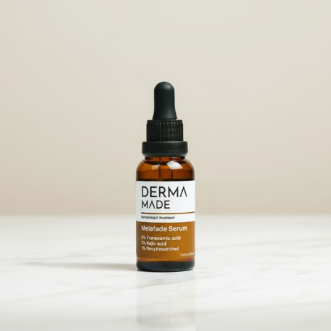 Derma Made Melafade Serum – Brightening Serum for Melasma and Dark Spots Derma Made Melafade Serum bottle with white and amber label placed on a marble counter against a soft beige background. The 4-inch amber glass dropper bottle contains Tranexamic Acid, Kojic Acid, and Hexylresorcinol to reduce melasma, dark spots, and hyperpigmentation.