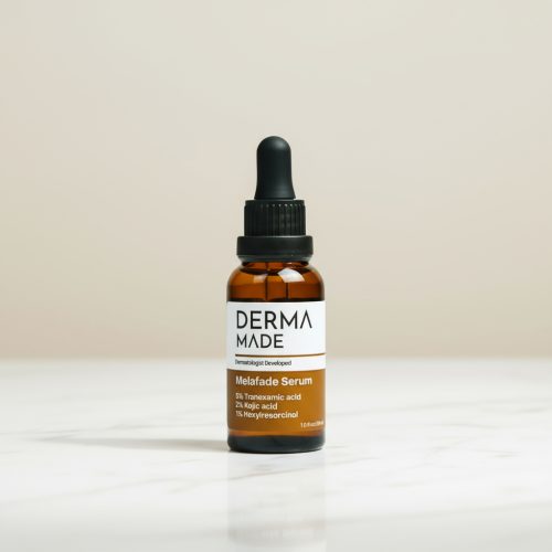 Derma Made Melafade Serum – Brightening Serum for Melasma and Dark Spots Derma Made Melafade Serum bottle with white and amber label placed on a marble counter against a soft beige background. The 4-inch amber glass dropper bottle contains Tranexamic Acid, Kojic Acid, and Hexylresorcinol to reduce melasma, dark spots, and hyperpigmentation.